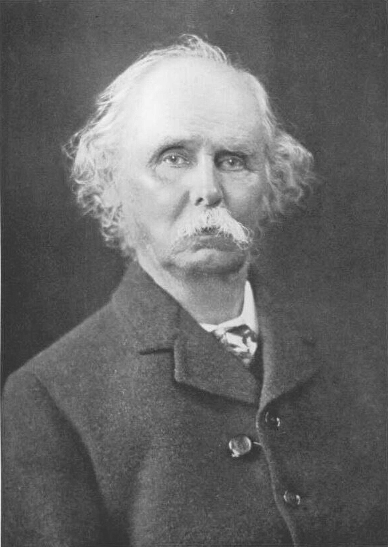 Retrato fotográfico del economista inglés Alfred Marshall, con barba blanca y traje oscuro.