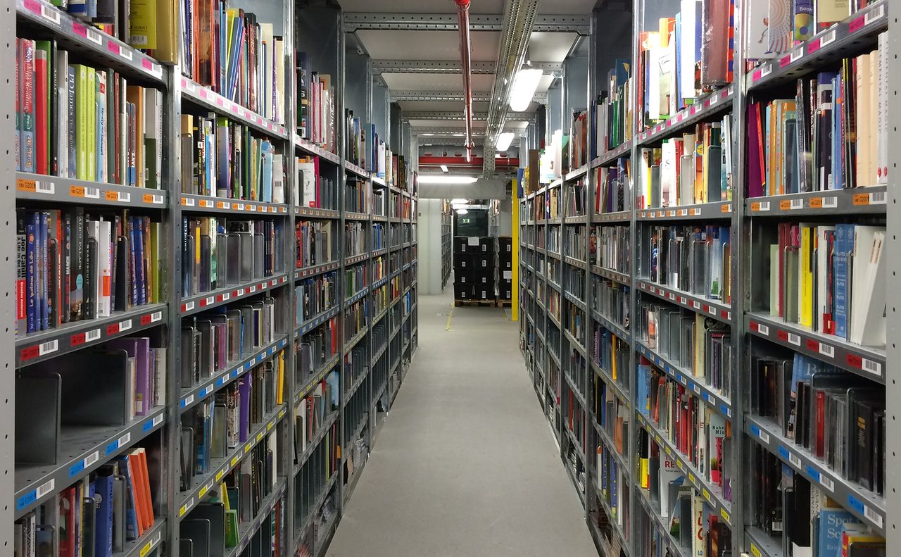 Interior de un gran almacén logístico con estanterías repletas de mercancía organizada en pasillos.