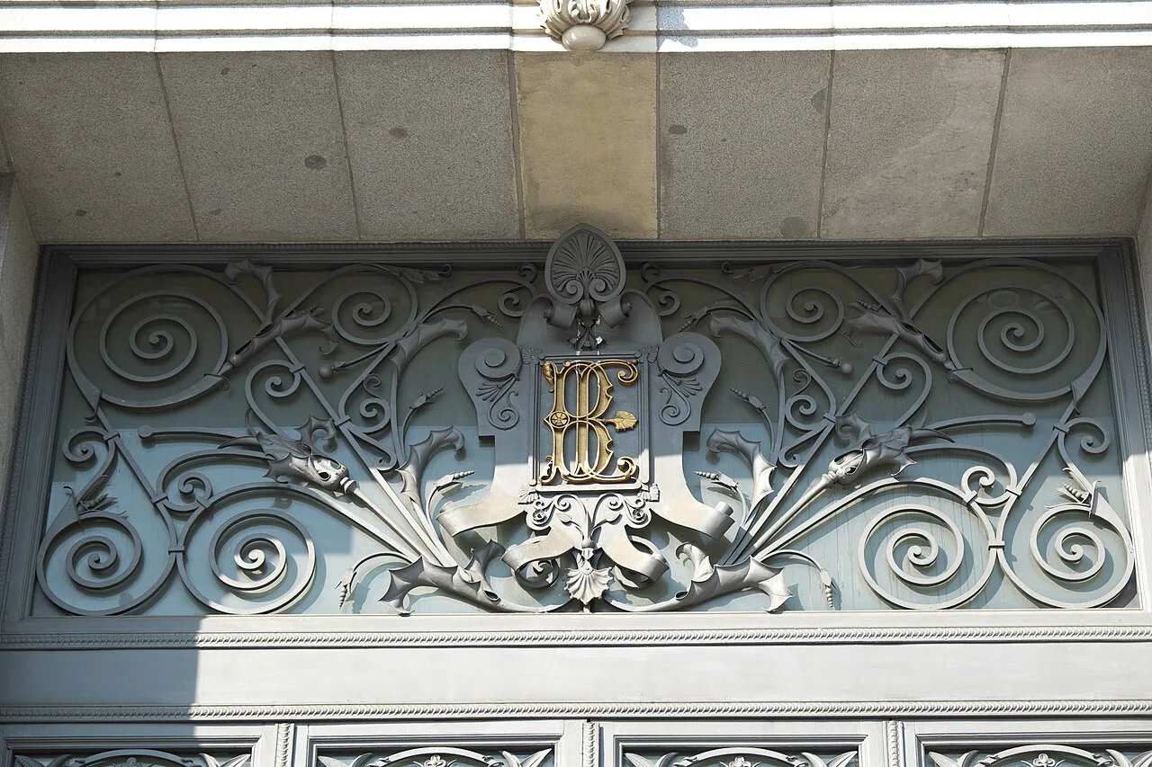 Detalle de la verja de hierro forjado del edificio del Banco de España, con las letras «BE» entrelazadas en el centro del óvalo decorativo.