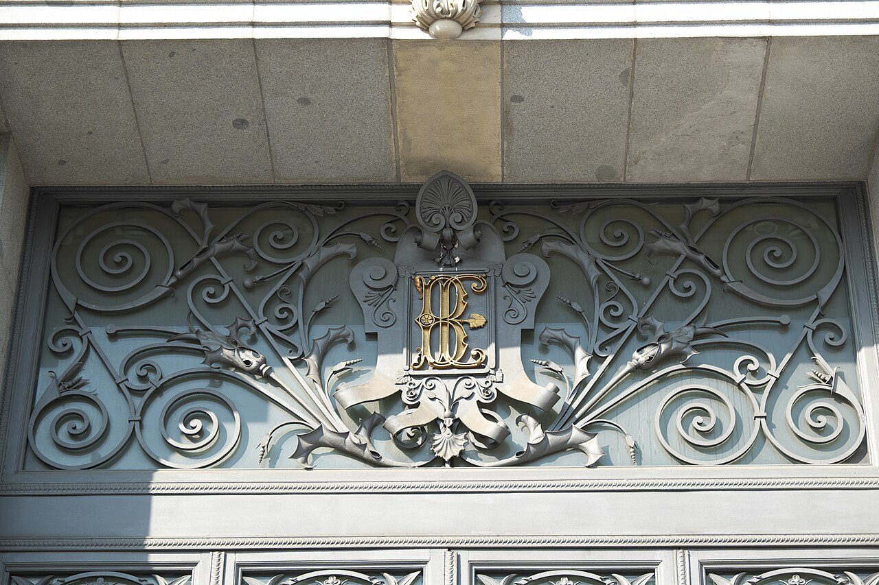 Detalle de la verja de hierro forjado del edificio del Banco de España, con las letras «BE» entrelazadas en el óvalo decorativo.