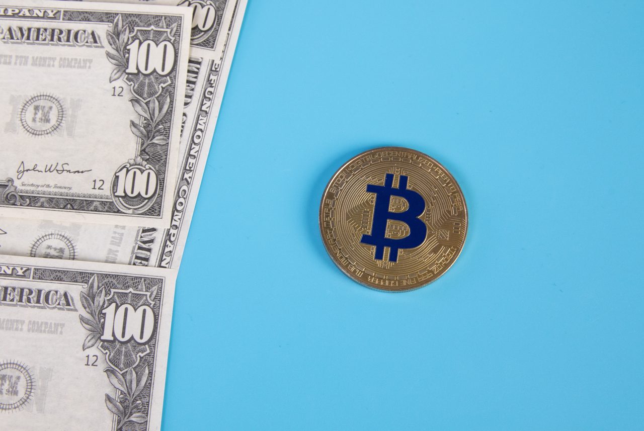 Representación física de una moneda de bitcoin con el símbolo BTC junto a billetes de euro y de dólar.
