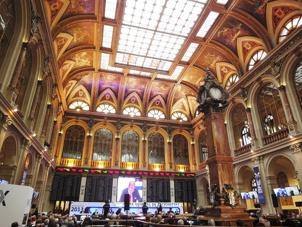 Sala principal de contratación del Palacio de la Bolsa de Madrid, con la pantalla central de cotizaciones y los puestos históricos de operadores bajo la bóveda decorada.