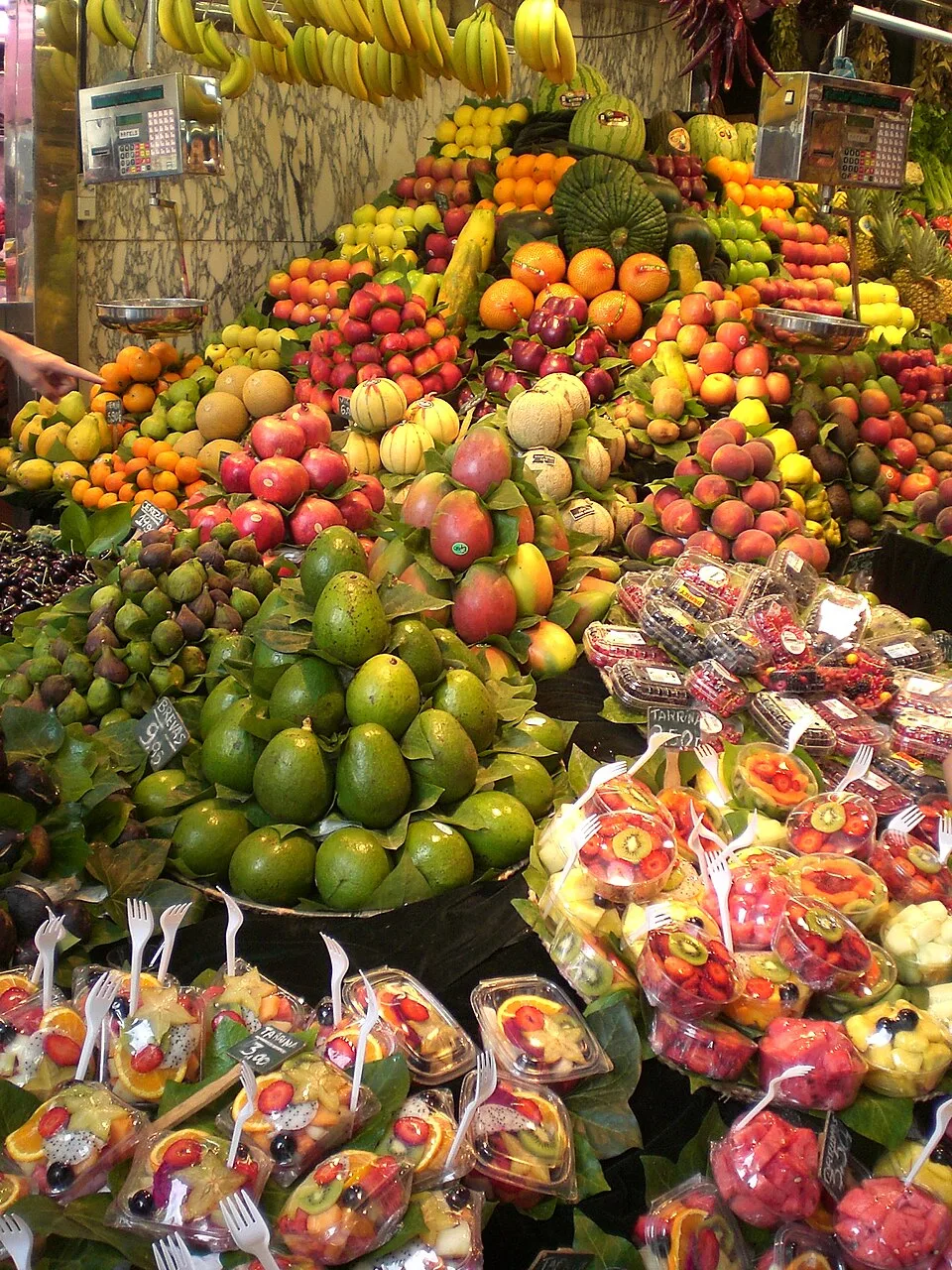 Puesto de fruta tropical en el Mercat de la Boqueria, en La Rambla de Barcelona, con cajas de productos de colores intensos y carteles de precios escritos a mano.