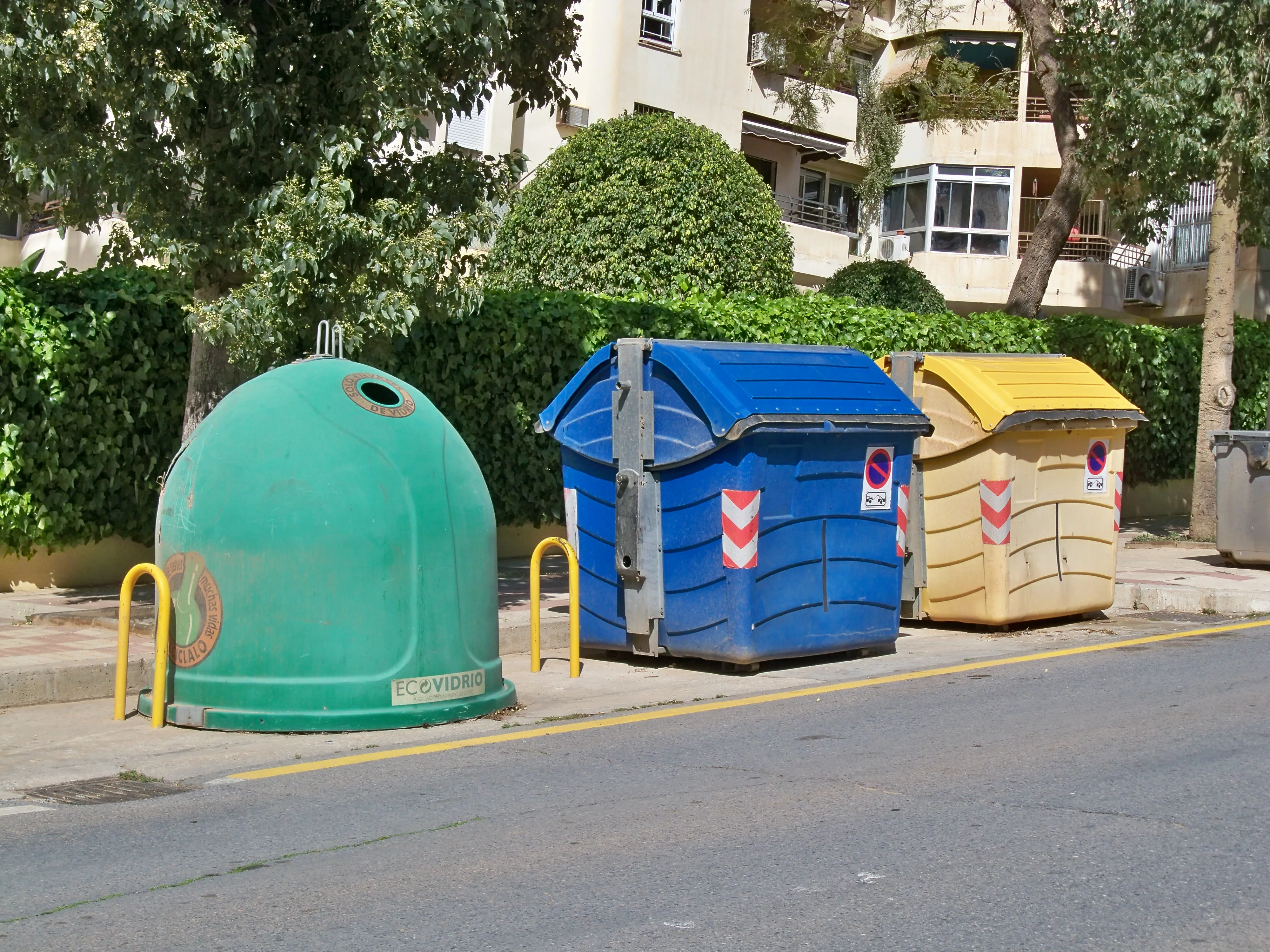 Fila de contenedores de reciclaje de distintos colores en una calle para separar vidrio, papel, envases y orgánico.