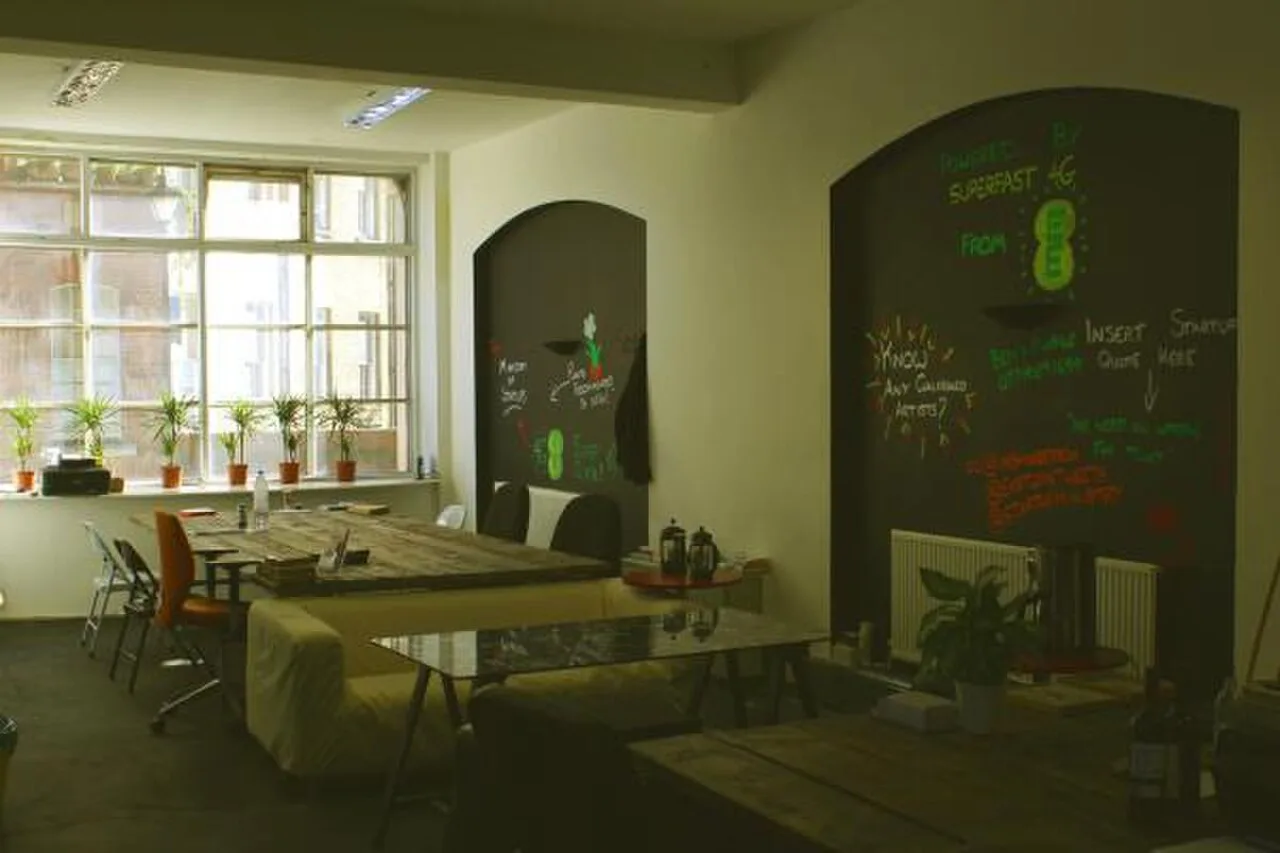 Espacio de coworking moderno con varias personas trabajando en mesas compartidas, ordenadores portátiles abiertos y ambiente colaborativo.
