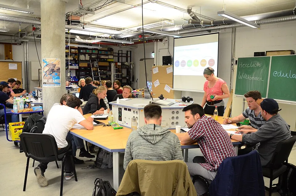 Sesión colaborativa de design thinking con participantes trabajando en grupo alrededor de mesas con materiales de papel y notas adhesivas.