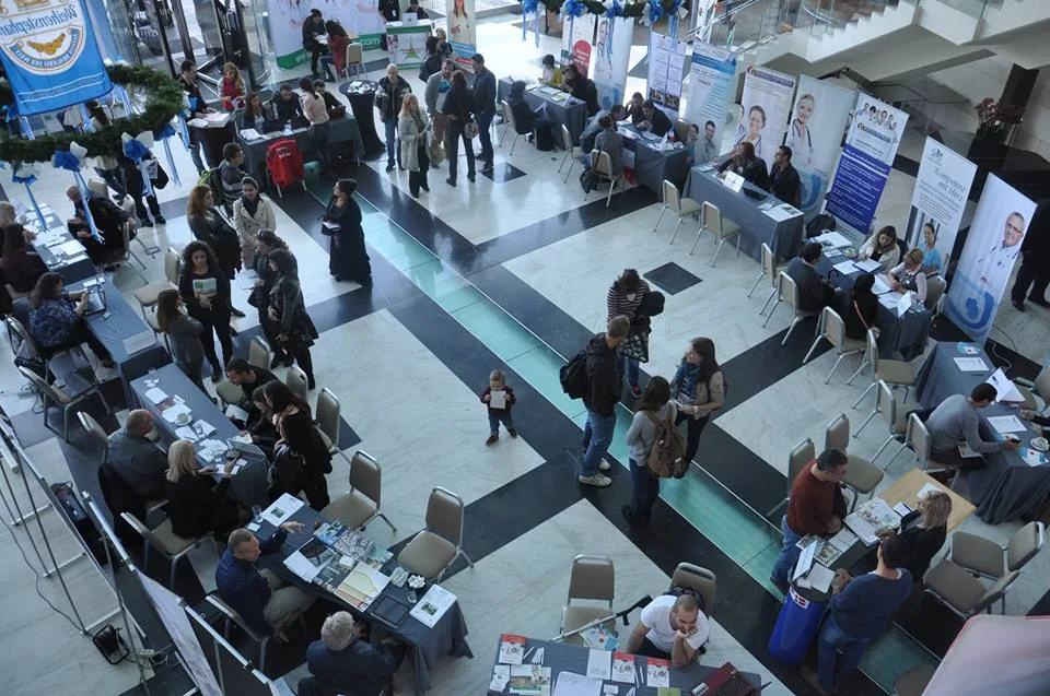 Visitantes consultando ofertas en un panel de una feria de empleo, con personal sanitario revisando puestos en el extranjero.