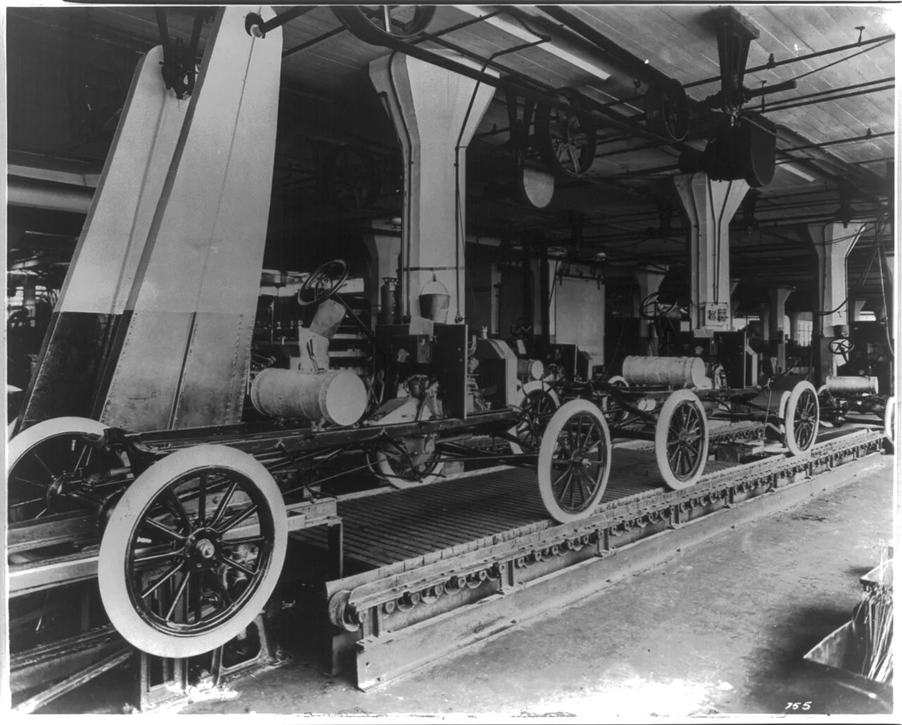 Fotografía de archivo de 1913 que muestra la cadena de montaje del Ford Model T en la planta de Highland Park, con chasis en distintas fases de ensamblaje sobre la cinta y operarios trabajando a lo largo de la línea.
