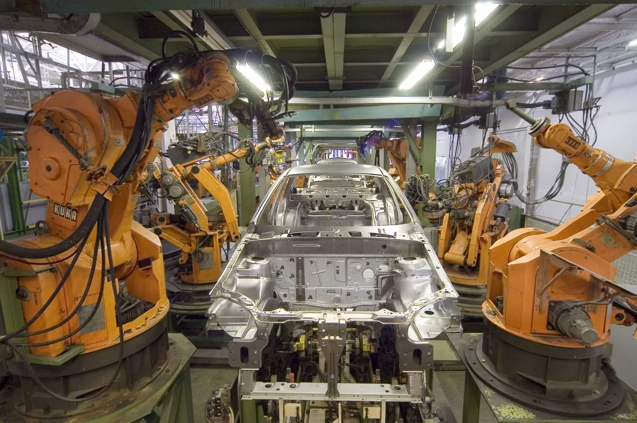 Hilera de brazos robóticos industriales naranjas de la marca KUKA dispuestos sobre una plataforma de exposición, con los manipuladores articulados en distintas posiciones.