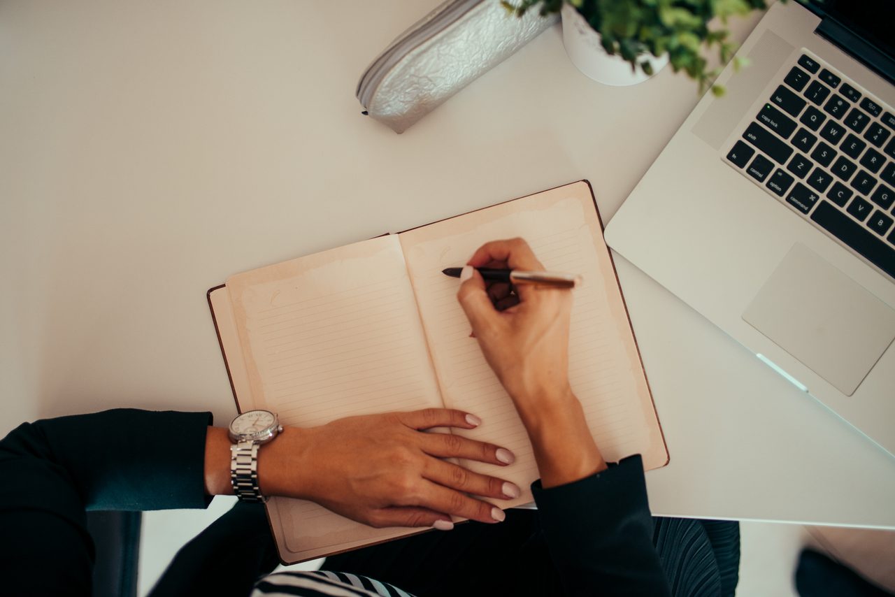 Persona tomando notas en una libreta mientras trabaja con un portátil en un espacio de trabajo moderno