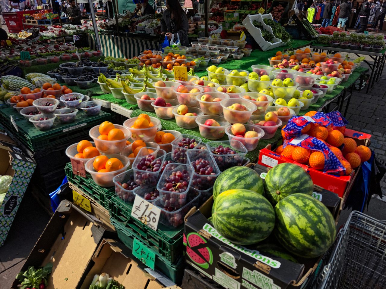 Puesto de fruta y verdura en un mercadillo al aire libre, con cajas de productos y precios a la vista