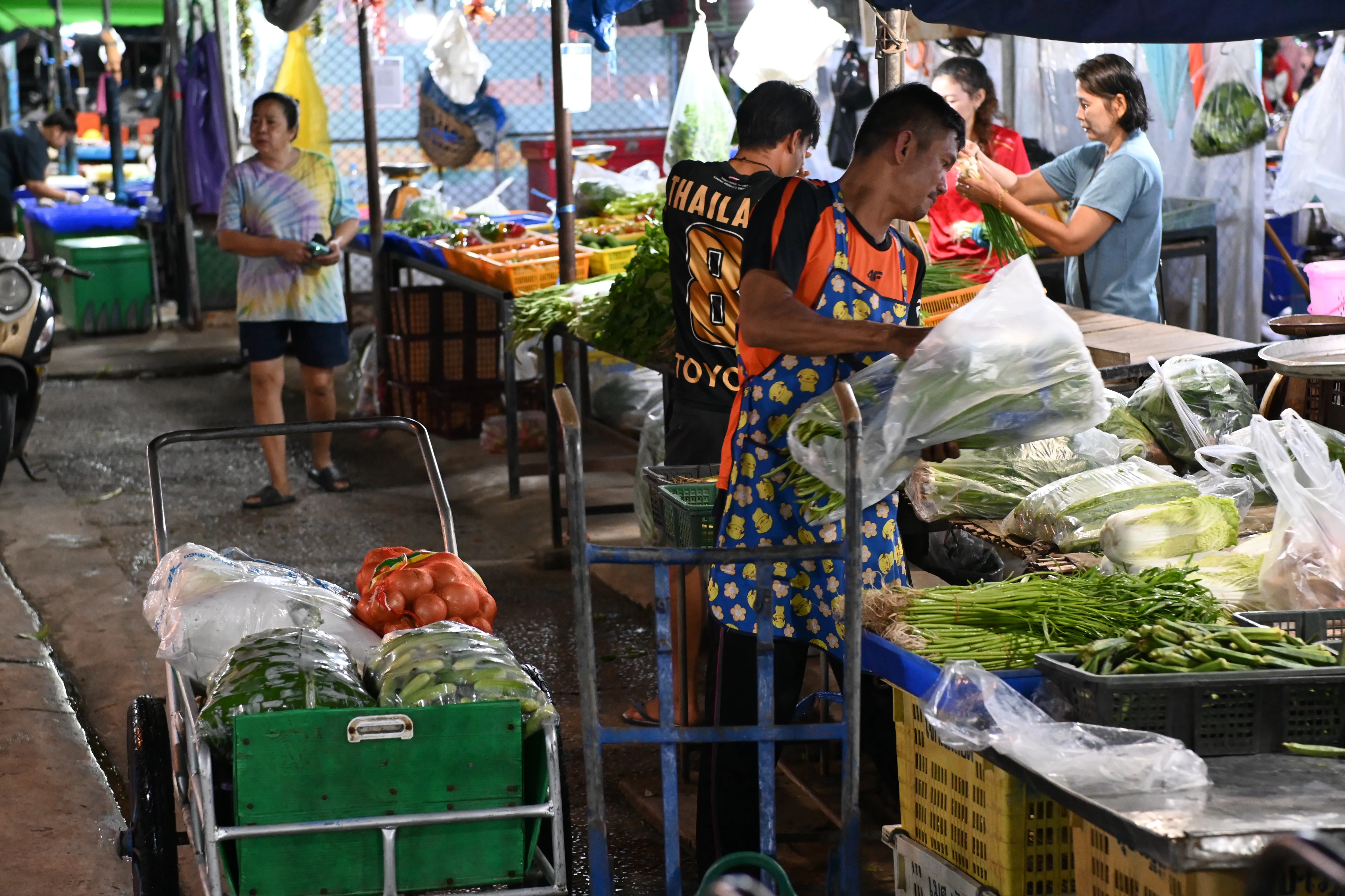 Vendedores colocando verdura fresca en una parada de mercado al aire libre, preparando el género antes de la llegada de los clientes.