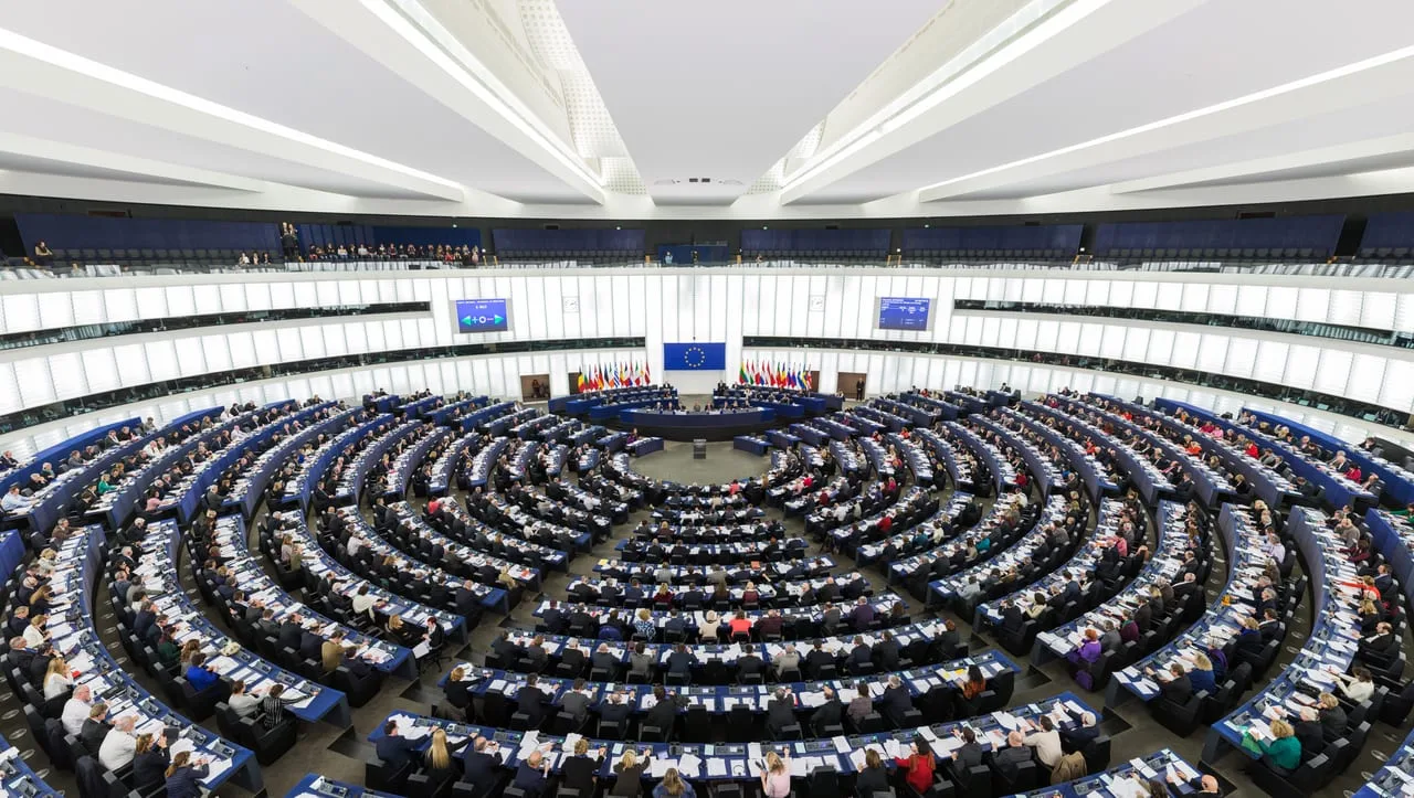 Hemiciclo del Parlamento Europeo en Estrasburgo lleno durante una sesión plenaria, con la bandera de la Unión al fondo.
