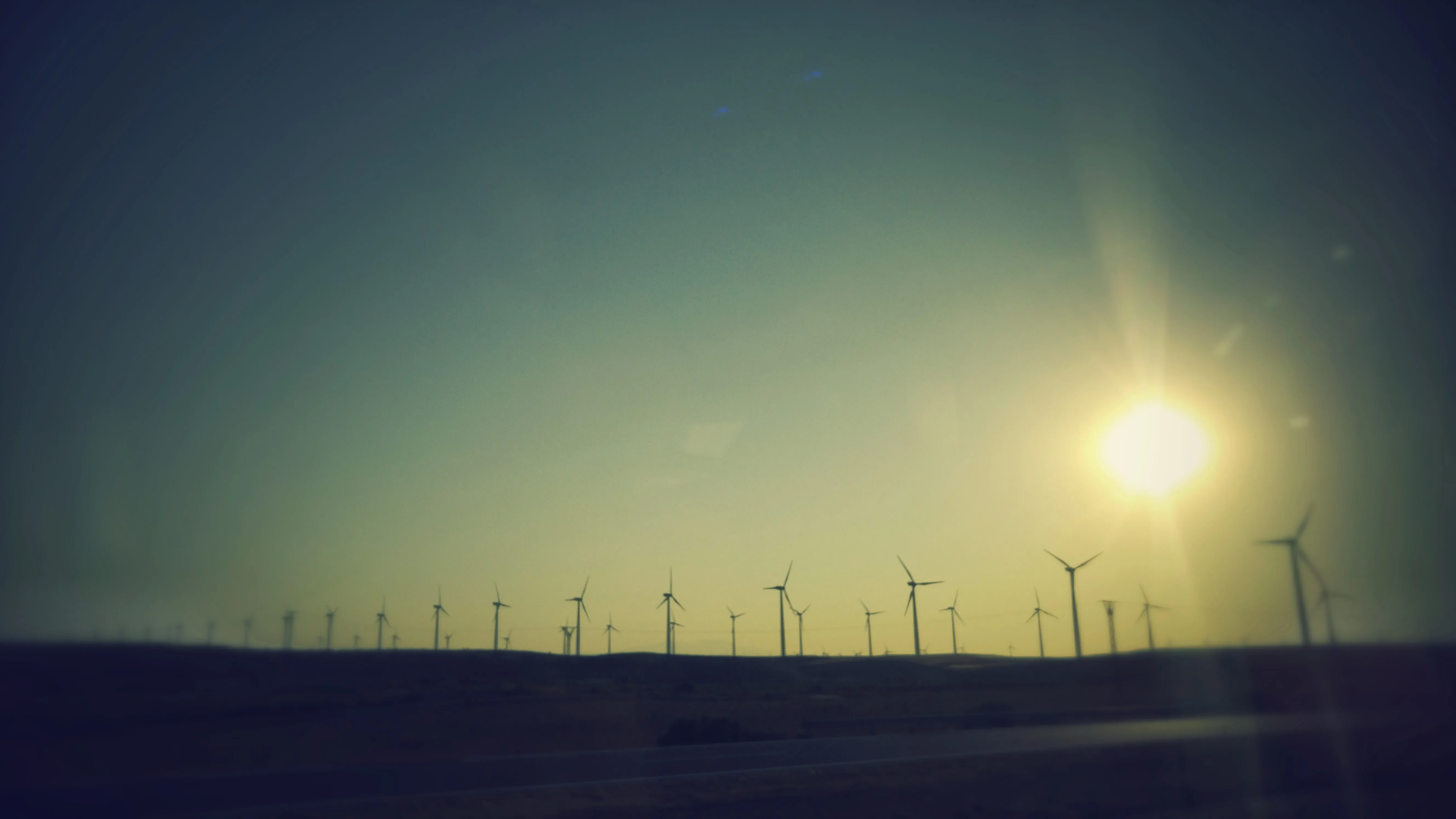 Parque eólico en un paisaje español al atardecer, con varios aerogeneradores recortados contra el cielo y la luz baja del sol.