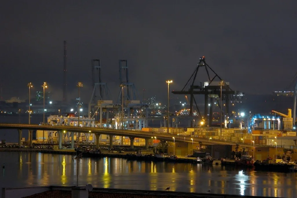 Amanecer en el puerto de Algeciras, con grúas de contenedores recortadas contra el cielo y filas de contenedores apilados en la terminal portuaria.