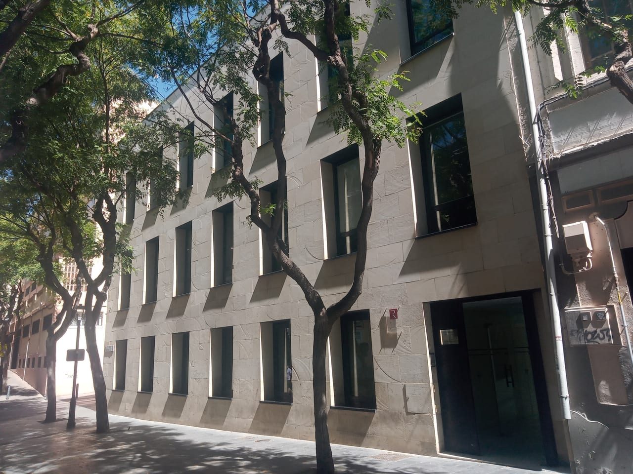 Fachada del edificio de un Registro de la Propiedad en una calle arbolada, con su placa junto a la entrada.