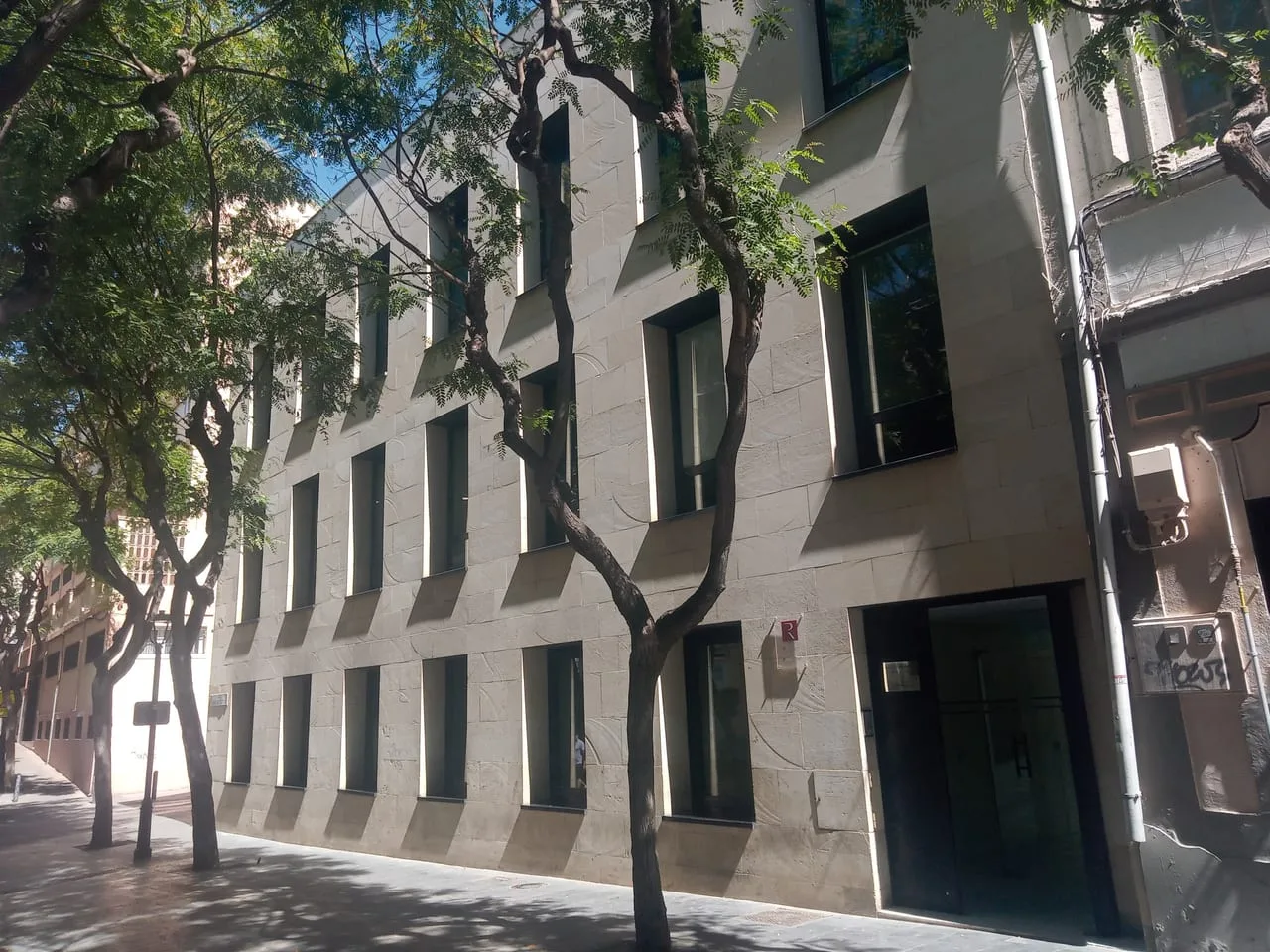 Fachada del edificio de un Registro de la Propiedad en una calle arbolada, con su placa junto a la entrada.