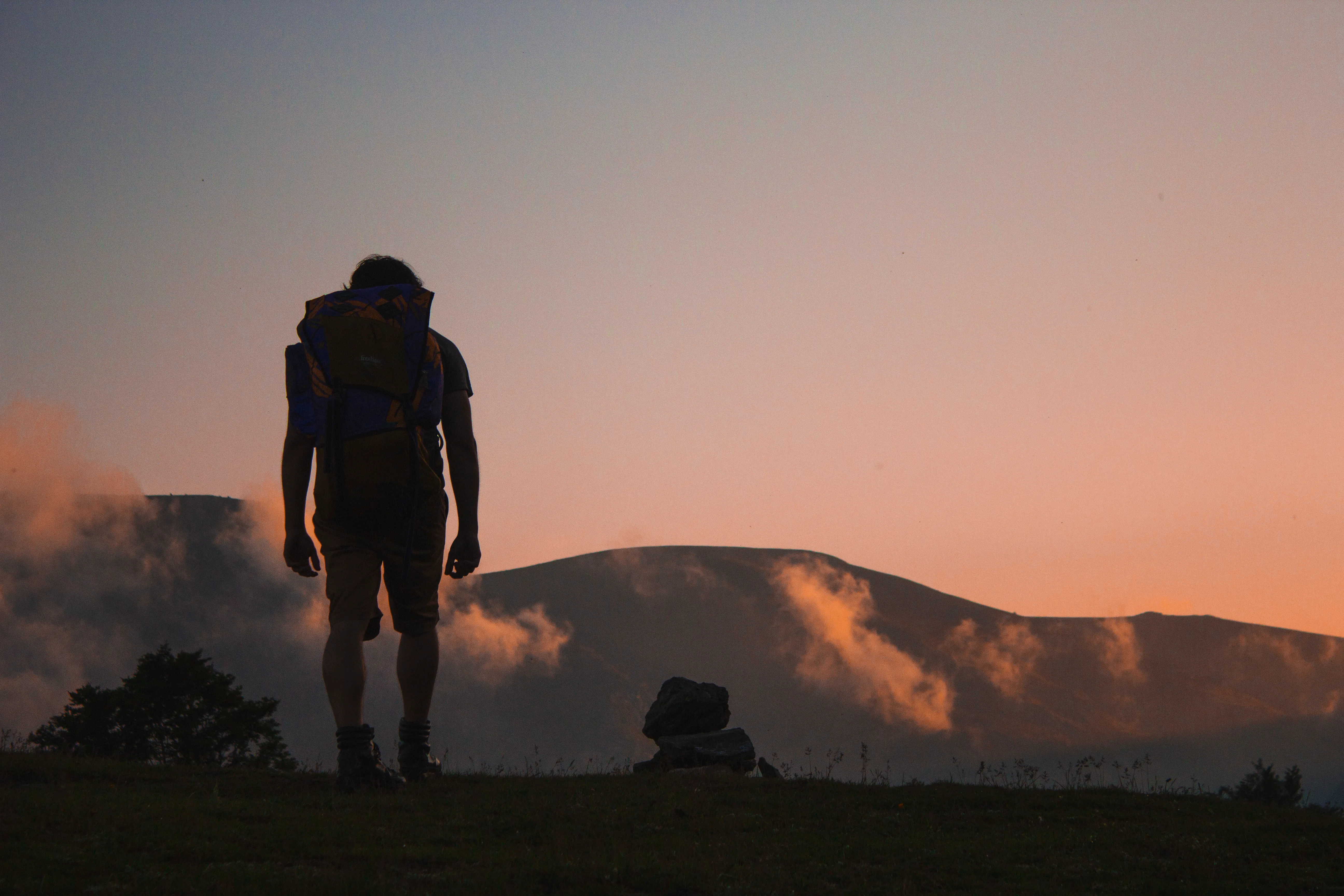 Persona joven contemplando el amanecer desde lo alto de una montaña, con un valle abierto al fondo.