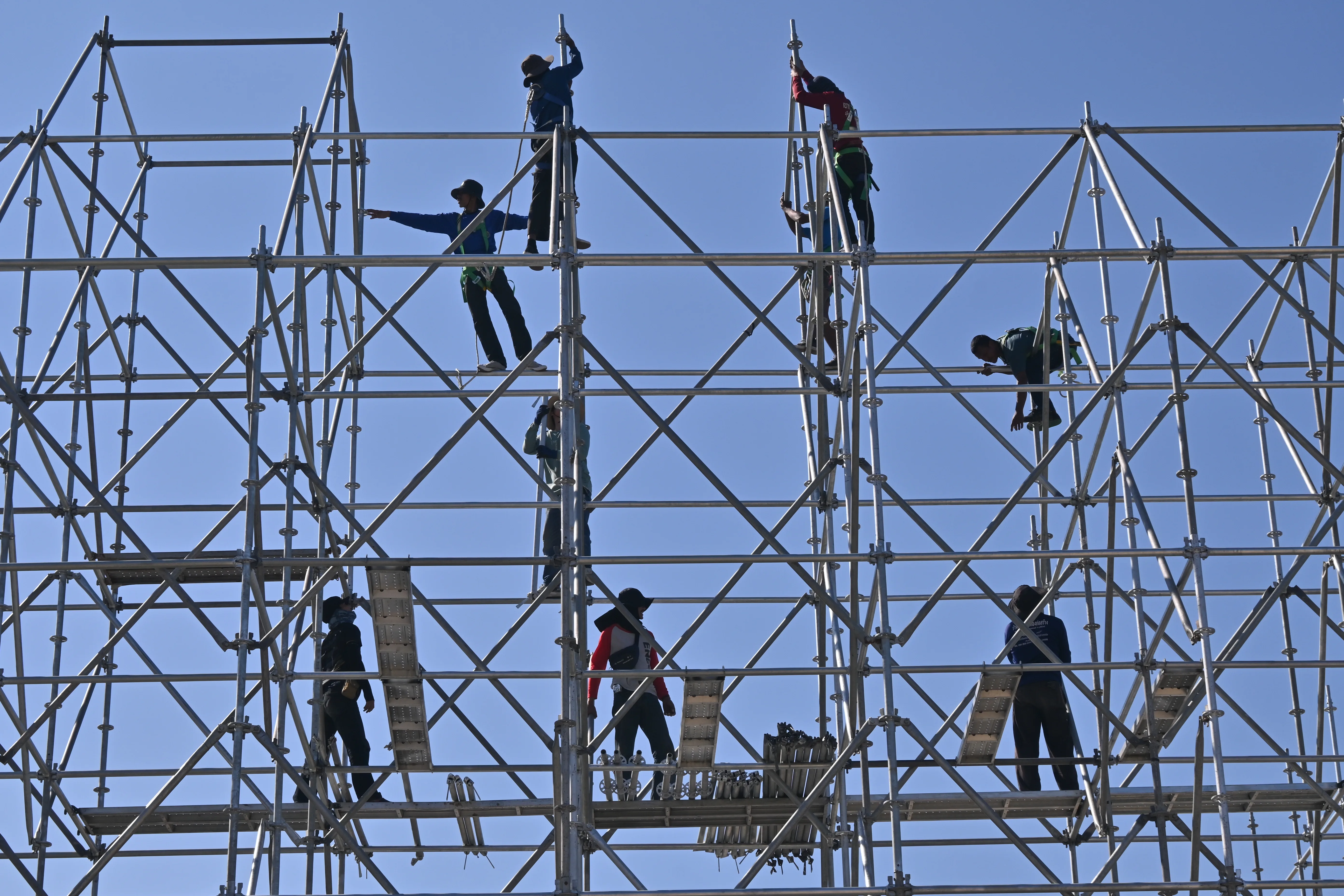 Trabajadores con casco, arnés y ropa de alta visibilidad montando un andamio metálico.