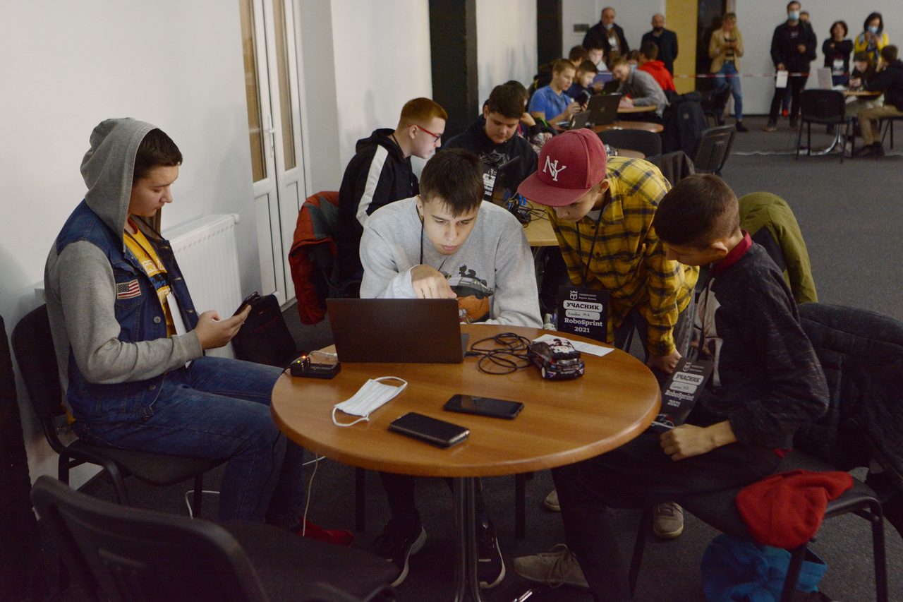 Grupo de jóvenes trabajando juntos alrededor de varias mesas en un proyecto en equipo