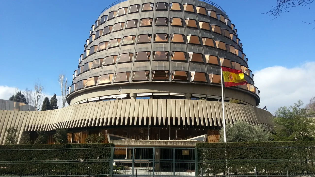 Sede del Tribunal Constitucional en Madrid, un edificio circular de hormigón y vidrio con la bandera de España delante.